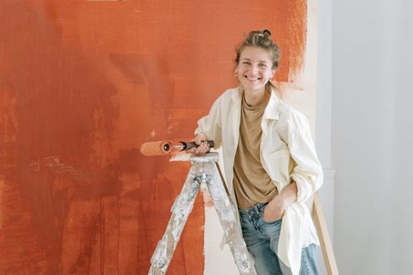 A woman on a ladder smiling and painting 600 Pexels
